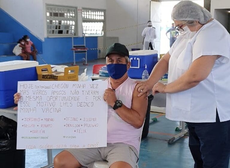 COMOVENTE: Idoso recebe vacina segurando cartaz com nomes de amigos que morreram vítimas de Covid-19